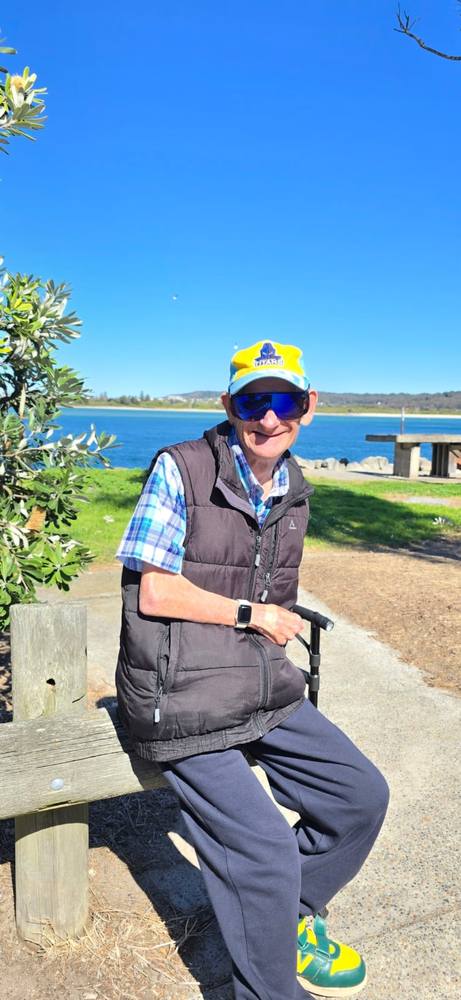 A man in a cap and sunglasses sitting on a bench by the water
