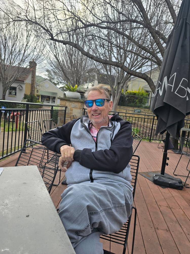 A man smiling at an outdoor café table