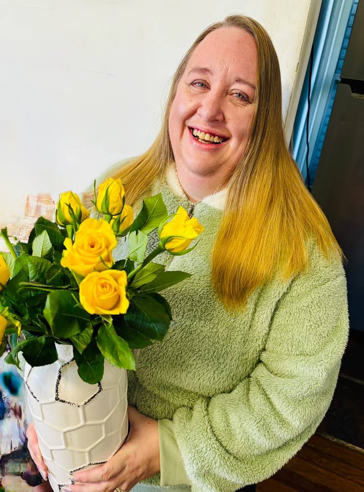 A woman smiling while holding a vase of yellow roses