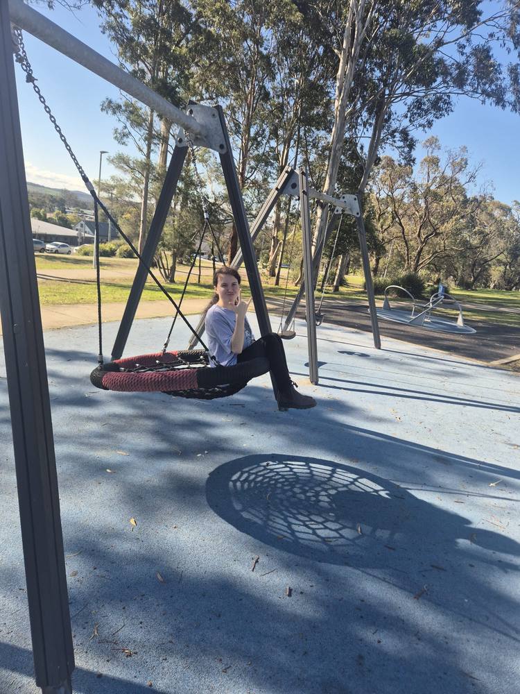 A young woman relaxing on a basket swing at a local park
